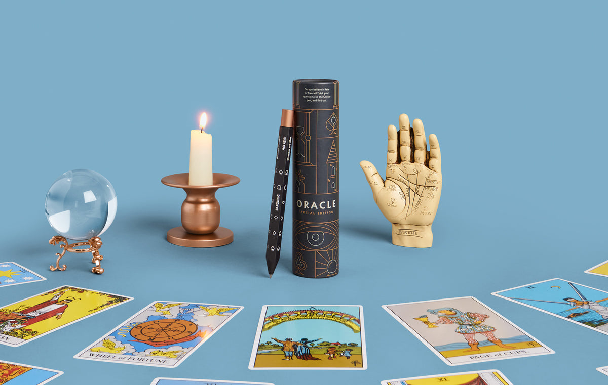 Oracle pen, crystal ball, candle, and hand-shaped object on a blue background with tarot cards.